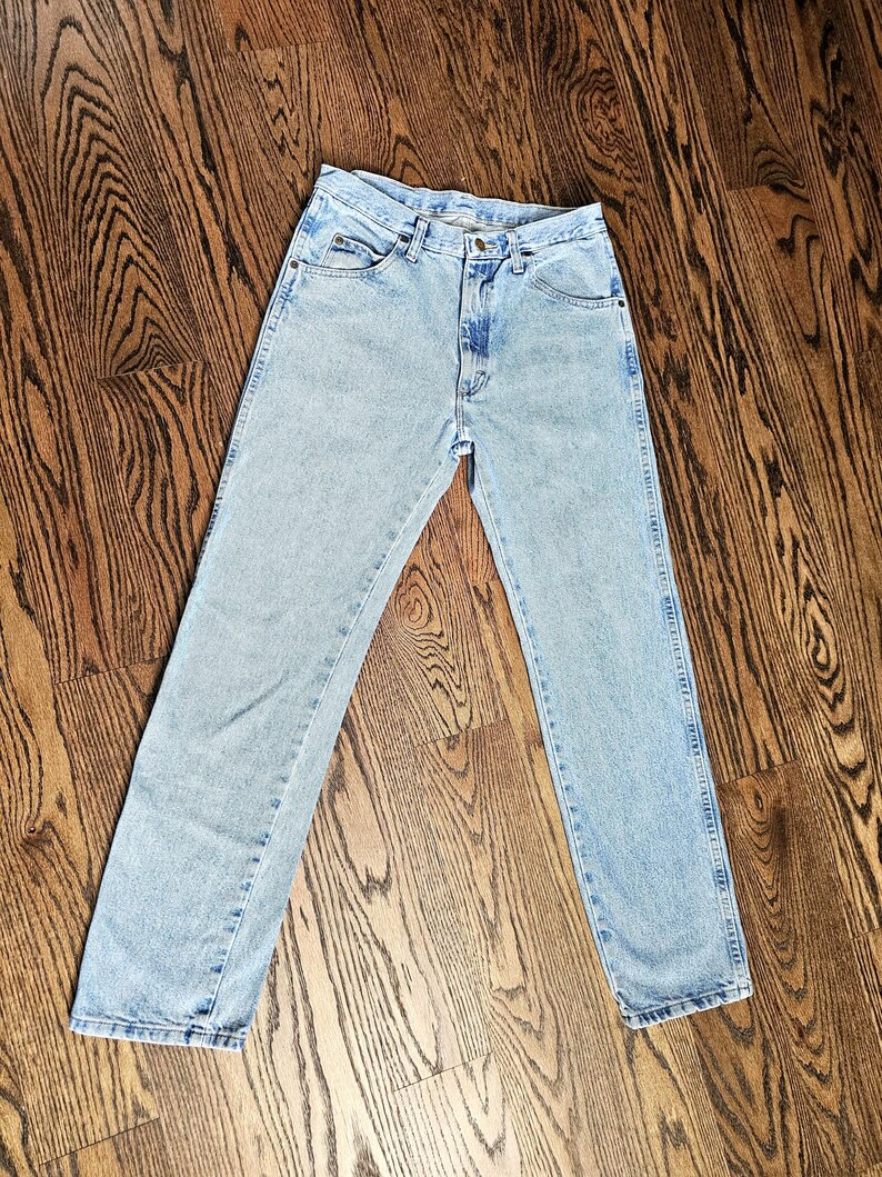May include: Light blue denim jeans with a classic five-pocket design. The jeans have a straight leg cut and a button and zipper closure. The denim has a faded wash, giving them a vintage look.