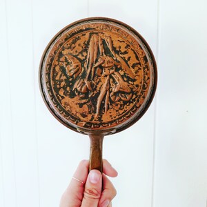 May include: A vintage copper pan with a floral design. The pan has a long handle and is in good condition.