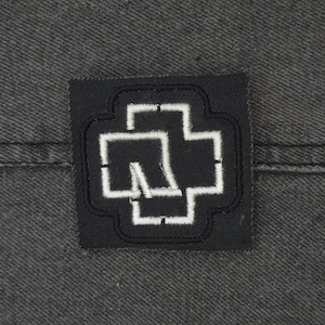 May include: Black and white embroidered patch with a stylized cross design. The cross is outlined in white and has a white shape inside.