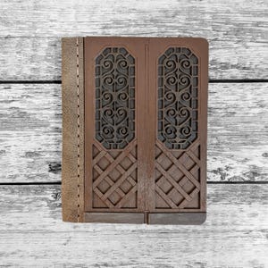 May include: A brown journal with a decorative wooden cover resembling a set of doors. The cover features intricate scrollwork and geometric patterns. The spine is a lighter brown leather with visible stitching.