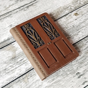May include: A brown leather-bound journal with a decorative wooden cover featuring a double door design with intricate metalwork.