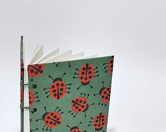 May include: A green and white journal with a ladybug pattern. The journal has a sewn binding and is closed.