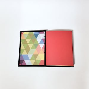 May include: A closed notebook with a black cover. The front cover has a geometric pattern of colorful triangles. The back cover is solid red.