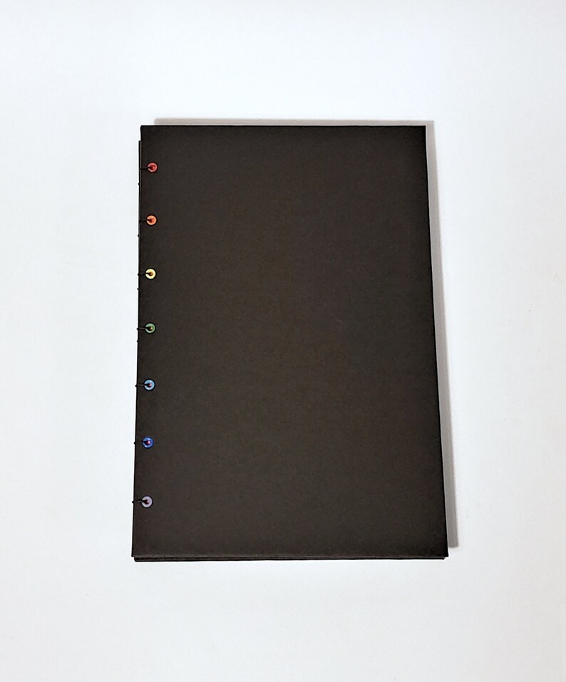 May include: A black notebook with a rainbow of colored stitching along the spine.