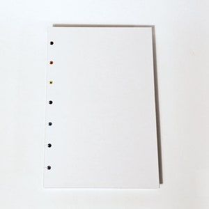 May include: A white notebook with a row of colorful dots along the left edge. The dots are black, orange, yellow, green, blue, and purple.