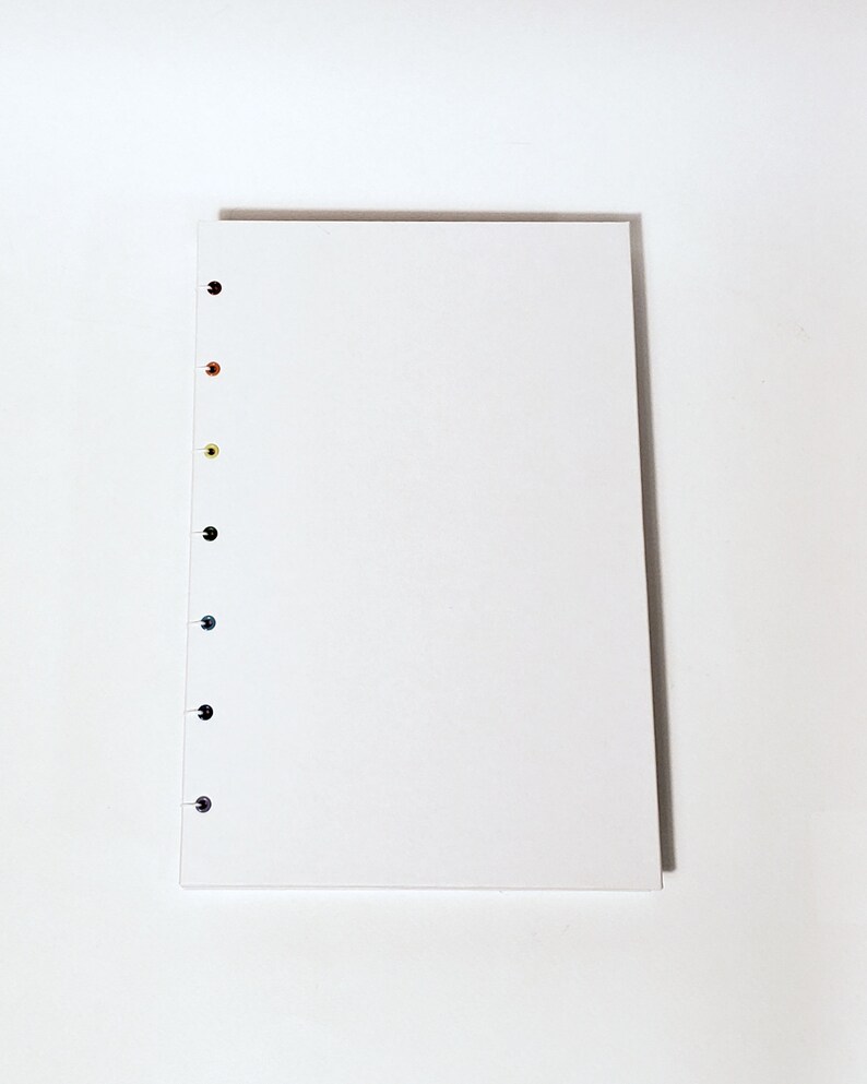 May include: A white notebook with a row of colorful dots along the left edge. The dots are black, orange, yellow, green, blue, and purple.