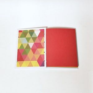 May include: A notebook with a geometric pattern on the front cover and a solid red back cover. The notebook is open to reveal blank pages.