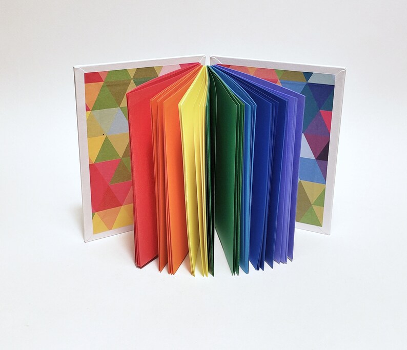May include: A small rainbow-colored book with a geometric pattern on the cover. The book is open and the pages are fanned out.