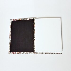 Pu&ograve; includere: Un quaderno aperto con una copertina nera e una pagina bianca. La copertina &egrave; decorata con un motivo colorato di persone e animali.