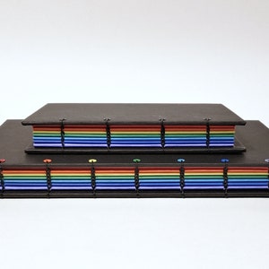 May include: Two black bound journals with rainbow colored pages. The smaller journal is stacked on top of the larger journal.