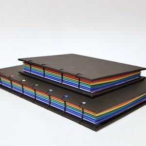 May include: Two black covered journals with rainbow colored pages. The smaller journal is stacked on top of the larger journal.