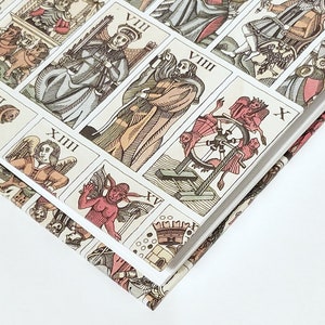 Pu&ograve; includere: Primo piano di un libro con un design colorato che presenta carte dei tarocchi. Il libro &egrave; aperto e le pagine sono aperte a ventaglio, rivelando le carte. Le carte sono illustrate con vari simboli e figure, tra cui uno scheletro, una ruota e un diavolo.