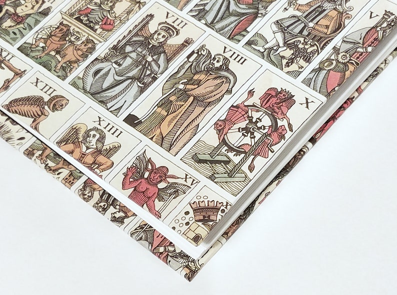 Pu&ograve; includere: Primo piano di un libro con un design colorato che presenta carte dei tarocchi. Il libro &egrave; aperto e le pagine sono aperte a ventaglio, rivelando le carte. Le carte sono illustrate con vari simboli e figure, tra cui uno scheletro, una ruota e un diavolo.