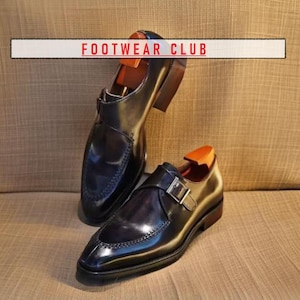 Könnte beinhalten: Zwei schwarze Lederschuhe mit Schnallenverschluss. Die Schuhe haben eine spitze Zehenpartie und eine polierte Oberfläche. Der Text "FOOTWEAR CLUB" ist im Hintergrund sichtbar.