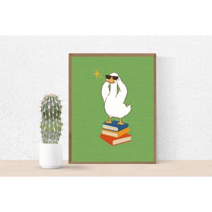 Peut inclure: Une affiche encadrée représentant une oie de dessin animé portant des lunettes de soleil, debout sur une pile de livres. L'oie est blanche avec un bec jaune et se détache sur un fond vert. Les livres sont bleus et orange.