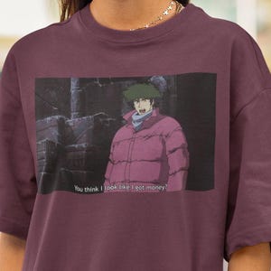 May include: Burgundy t-shirt featuring a rectangular graphic from an anime. The graphic shows a character in a pink jacket with the text "You think I look like I got money?" printed below. The person in the image is wearing black sunglasses.