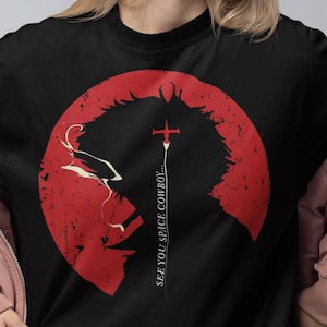 May include: Black t-shirt featuring a red graphic of a character silhouette within a red circle, with the text "SEE YOU SPACE COWBOY" in white. The person is wearing a pink jacket and black shorts.