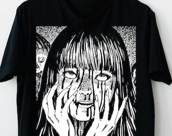 May include: Black t-shirt featuring a black and white illustration of a person with long hair, tears streaming down their face, and hands covering their face. The design has a manga or anime style.