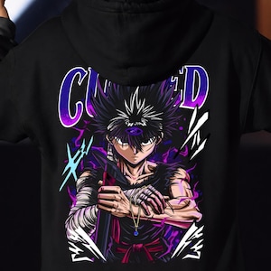 Peut inclure: Un sweat à capuche noir avec une impression graphique au dos représentant un personnage d'anime aux cheveux noirs hérissés, un troisième œil sur le front et les bras bandés. Il tient une épée, entouré d'énergie violette et du texte CURSED.