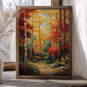 May include: A framed landscape painting of an autumn forest scene. The artwork features a path winding through trees with vibrant red, orange, and yellow foliage. The painting is displayed on a wooden surface.