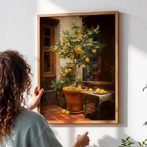May include: A framed artwork depicting a lemon tree in a terracotta pot, with ripe yellow lemons. The painting is set in a courtyard with a table and additional lemons. The artwork is being hung on a white wall.