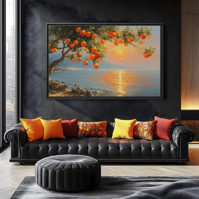 May include: A framed painting of an orange tree with ripe fruit hanging over a body of water at sunset. The painting hangs above a black leather sofa with colorful throw pillows and a black ottoman. The room has dark walls.