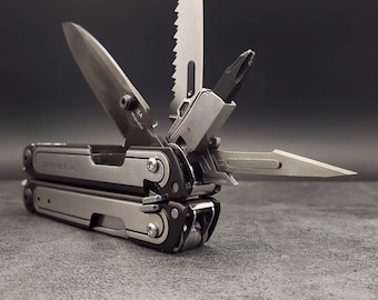 Puede incluir: Una herramienta multiusos plateada con mango negro y una variedad de herramientas, incluyendo una sierra, un cuchillo y un destornillador. La herramienta está abierta y la hoja está extendida. El texto "Leatherman  J.K.  USA" es visible en el mango.