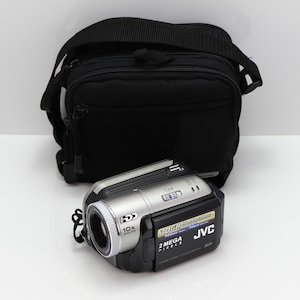 Könnte beinhalten: Ein silber-schwarzer JVC-Camcorder mit 10-fach optischem Zoomobjektiv, 30-GB-Festplatte und 2-Megapixel-Auflösung, begleitet von einer schwarzen Reißverschluss-Tragetasche mit verstellbarem Schultergurt zur Aufbewahrung und zum Transport.