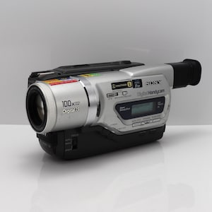 May include: A silver and black Sony Digital Handycam camcorder featuring a 100x digital zoom lens, Digital8 recording technology, a small LCD status display, NightShot capability, and a black viewfinder eyepiece on the rear of the device.