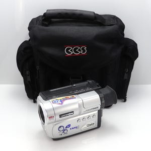 May include: A silver Medion camcorder featuring a 22x optical zoom lens, 880x digital zoom, and Hi8 recording functionality, placed in front of a black CCS branded carrying bag with a top handle and side pockets for equipment storage and transport.
