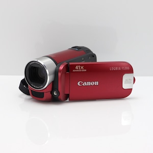 Op de afbeelding: Een rode Canon Legria FS306 camcorder met een zilverkleurige lenscilinder. Het zijpaneel bevat de tekst Canon, 41x Advanced Zoom en Legria FS306, samen met een icoon voor een SD-geheugenkaartsleuf. Het apparaat heeft een compact, horizontaal ontwerp.