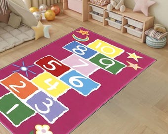 May include: A pink play mat with a hopscotch design featuring numbers 1 through 10. The mat has a colourful design with yellow, green, blue, red, and purple squares. There are also stars and a crescent moon on the mat.