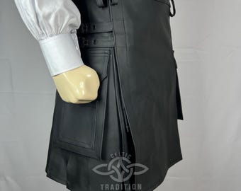 Könnte beinhalten: Schwarzer Lederkilt mit Falten und Taschen. Der Kilt hat verstellbare Riemen und Knöpfe. Das Celtic Tradition-Logo ist unten rechts sichtbar. Getragen mit einem weißen Hemd und weißen Socken.