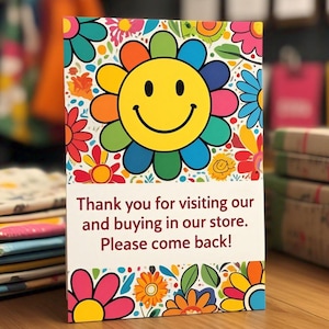 Puede incluir: Una tarjeta de agradecimiento rectangular con una cara sonriente amarilla grande rodeada de p&eacute;talos de flores coloridos. La secci&oacute;n inferior tiene un fondo blanco con el texto: Thank you for visiting our and buying in our store. Please come back!