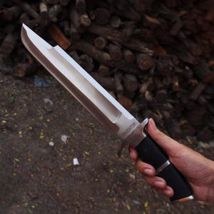 May include: A silver knife with a black handle. The knife has a long blade and a serrated edge. The handle has a black grip and a silver metal guard. The knife is labeled "PREDATOR" on the blade.