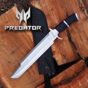 May include: A silver and black hunting knife with a black leather sheath. The knife has a black handle and a silver blade with the word "PREDATOR" etched on it.