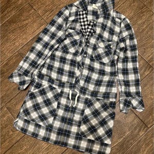 May include: A white and black plaid shirt with long sleeves and a drawstring waist. The shirt has a button-up front and two pockets.