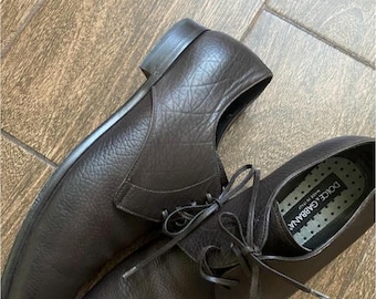 May include: A pair of brown leather lace-up shoes with a black and white label that reads "DOLCE & GABBANA" and "MADE IN ITALY".