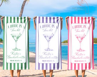 May include: Three beach towels with vertical stripes in green, purple, and pink. Each towel features a cocktail glass illustration and the text "A Bride in a Tini bit" and "Katie's Bachelorette, Miami Beach, FL."
