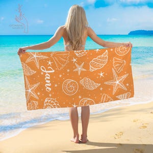Pu&ograve; includere: Asciugamano da spiaggia arancione con un motivo di conchiglie e stelle marine bianche. L'asciugamano ha il nome "Jane" scritto su di esso.