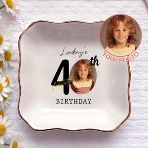 May include: A white ceramic dish with a gold rim, featuring a photo and text that reads "Lindsay's 40th Birthday." The dish has a square shape with gently curved edges. The photo is of a person with curly hair.