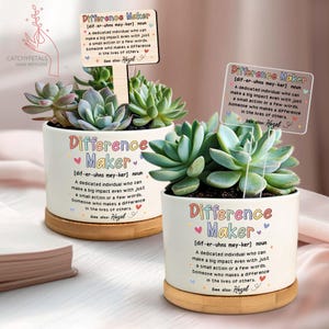 May include: Two white ceramic pots with succulents, each displaying the text "Difference Maker" and a definition. The pots are on bamboo saucers. One pot has a wooden sign that reads "Difference Maker".