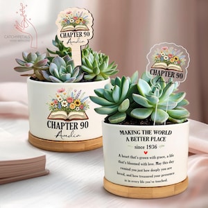 May include: Two white ceramic succulent planters with bamboo bases. Each planter features a floral design and the text "CHAPTER 90 Amelia." One planter includes the text "MAKING THE WORLD A BETTER PLACE since 1936."