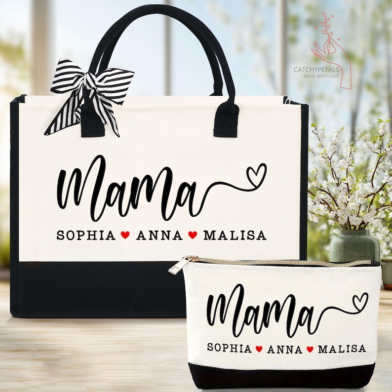 May include: A canvas tote bag and matching cosmetic bag set. The bags are off-white with black accents and handles. The word "Mama" is printed in black script, along with three names and hearts. A black and white striped bow adorns the tote bag.