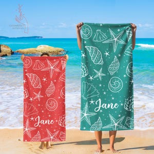 Pu&ograve; includere: Due asciugamani da spiaggia con un motivo a conchiglie e stelle marine. Gli asciugamani sono rossi e turchesi con contorni bianchi. Il testo "Jane" &egrave; scritto su ogni asciugamano.