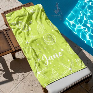 Pu&ograve; includere: Un asciugamano da spiaggia verde con un motivo a conchiglie e stelle marine bianche. L'asciugamano ha il nome "Jane" scritto in lettere bianche corsive.