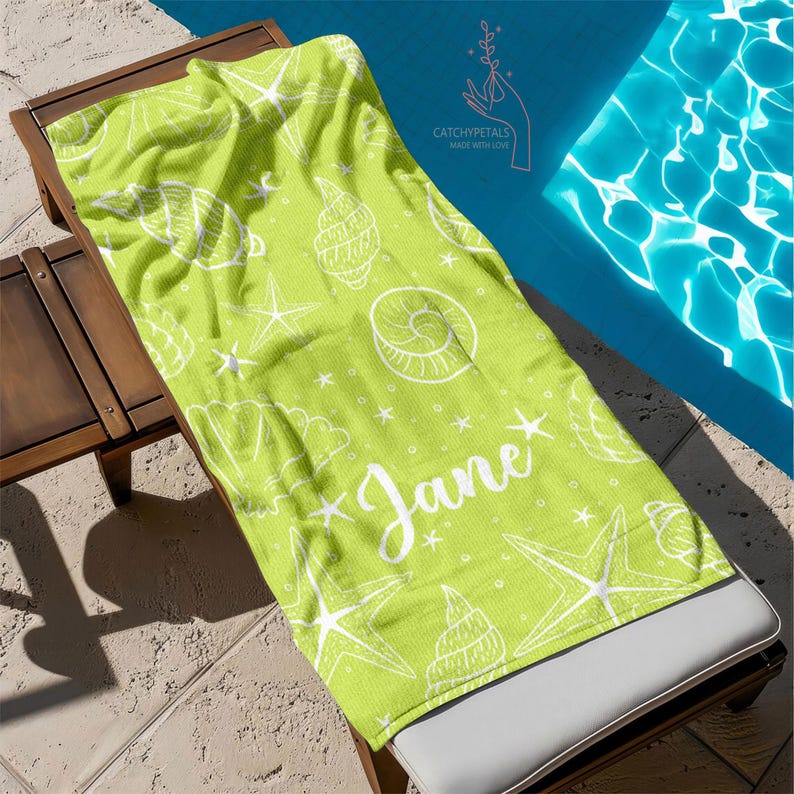 Pu&ograve; includere: Un asciugamano da spiaggia verde con un motivo a conchiglie e stelle marine bianche. L'asciugamano ha il nome "Jane" scritto in lettere bianche corsive.