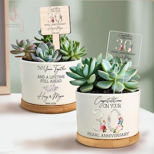 May include: Two succulent plants in white ceramic pots with bamboo saucers. The pots have text that reads "30 Years Together" and "Congratulations on your 30th Pearl Anniversary". Each pot has a decorative sign.