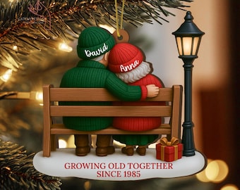 May include: A Christmas tree ornament depicting a couple on a bench, with the names "David" and "Anna" on their hats. The ornament includes a gift box and a lamppost, with the text "GROWING OLD TOGETHER SINCE 1985".