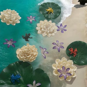 May include: A white and green resin art piece with a beach scene. The scene includes white sand, blue water, and green lily pads with frogs and flowers.